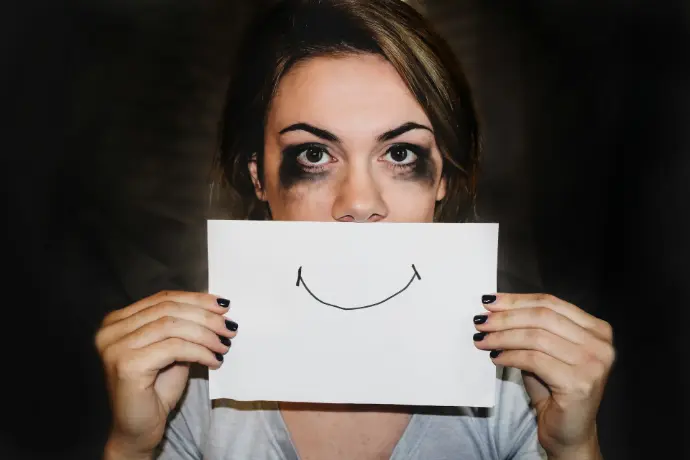 Personne triste avec feuille sourire Jeune femme à l'air triste tenant une feuille avec un sourire devant sa bouche