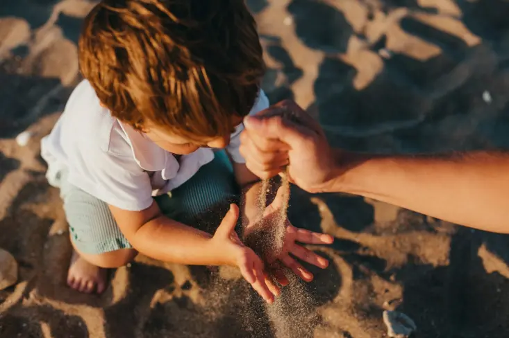 Enfant jouant Enfant jouant dans le sable et recevant une poignée de sable de la part d'une main adulte